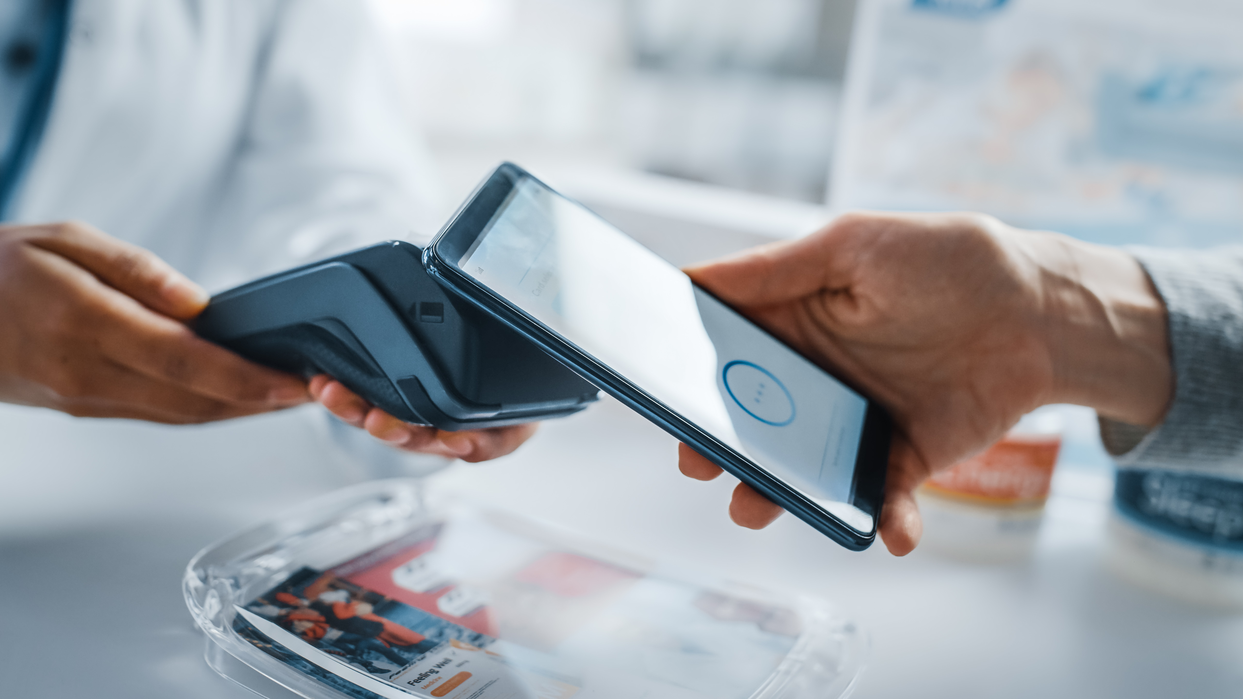 A customer pays at a store using their smartphone, while the merchant holds a Point-of-Sale terminal.