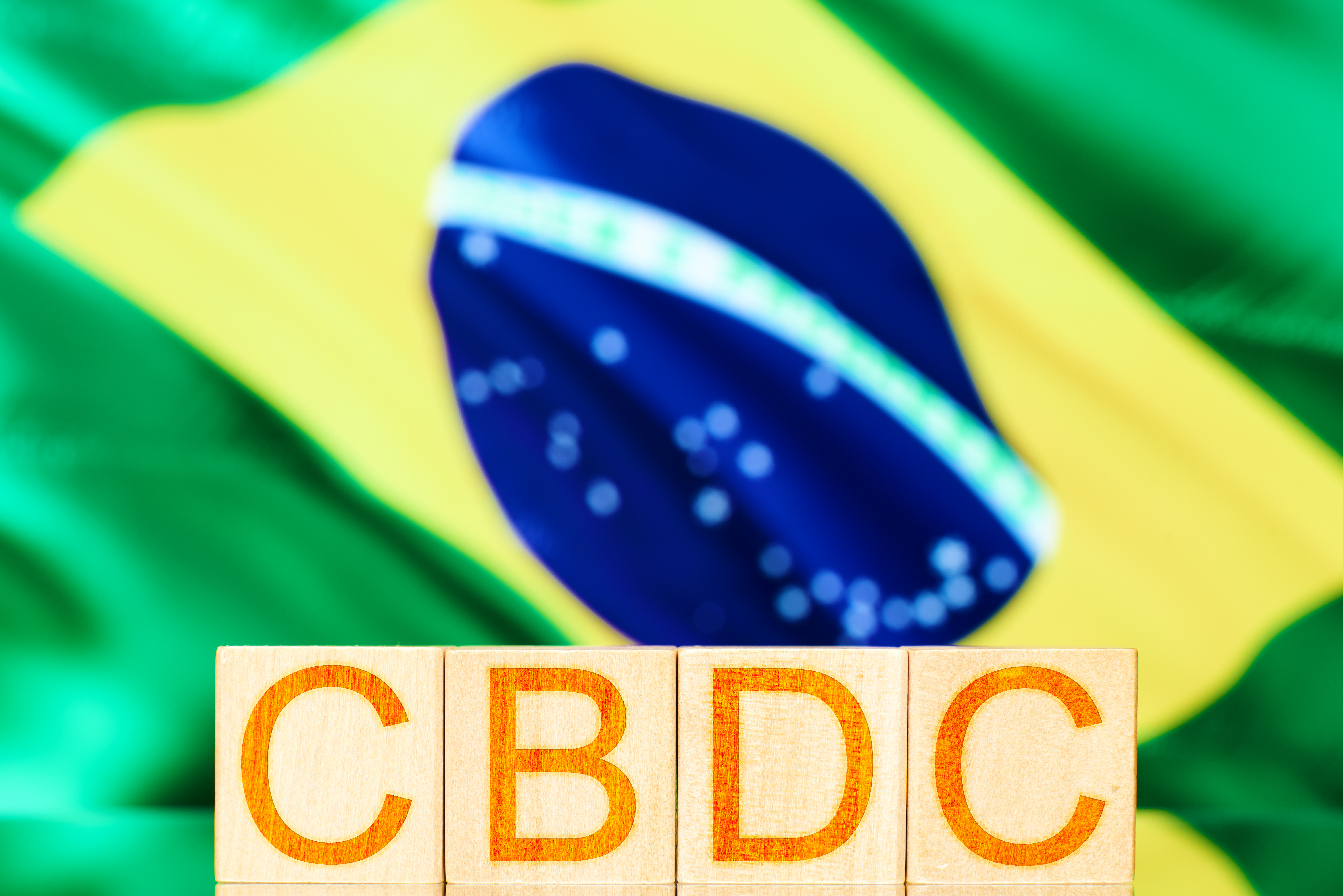 Wooden blocks emblazoned with the letters CBDC against a backdrop of the Brazilian flag.