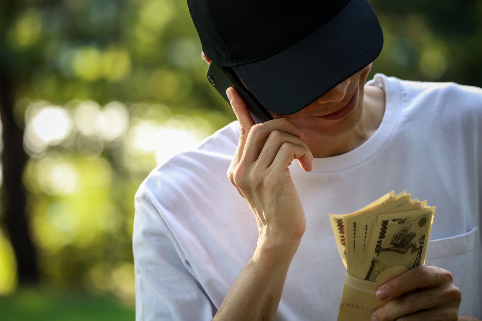 A young man speaks on a mobile phone while looking at an envelope full of Japanese banknotes.