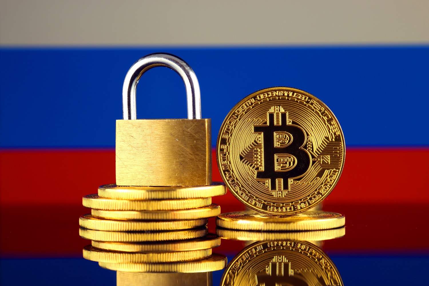 Piles of coins representing Bitcoin and a padlock against the backdrop of the Russian flag.
