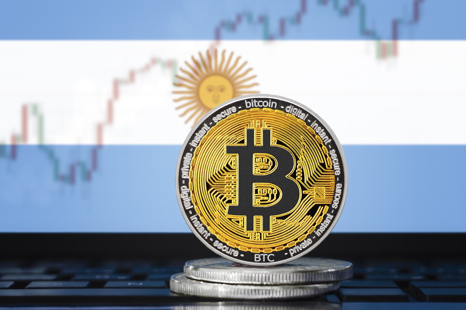 Metal tokens representing Bitcoin against the background of the flag of Argentina and a price chart.