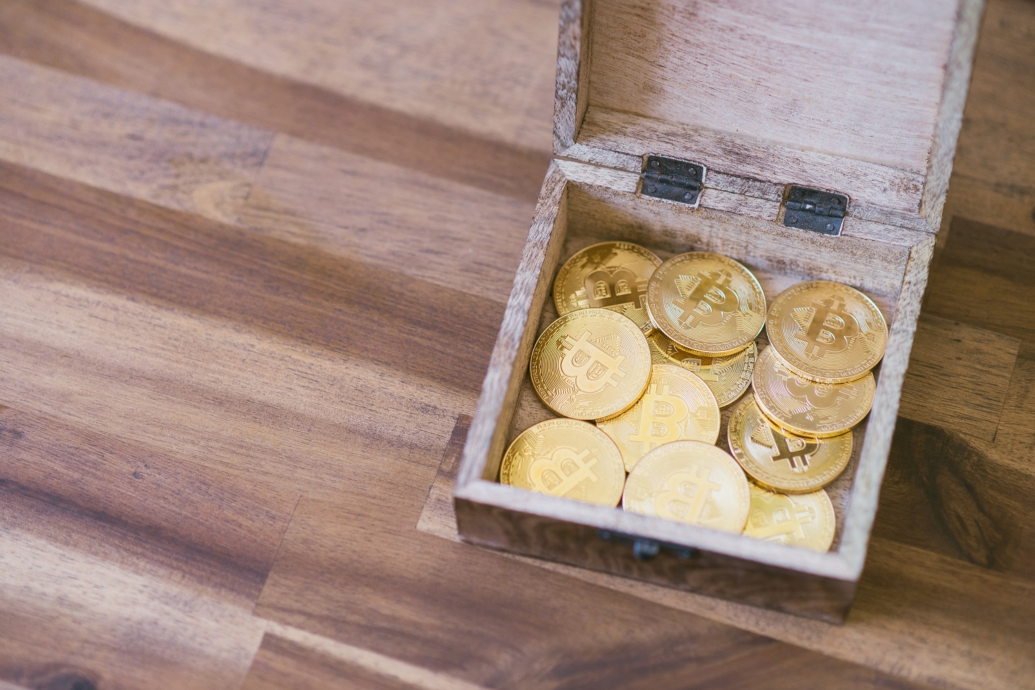 A wooden box containing golden tokens intended to represent Bitcoin on a wooden floor or table.