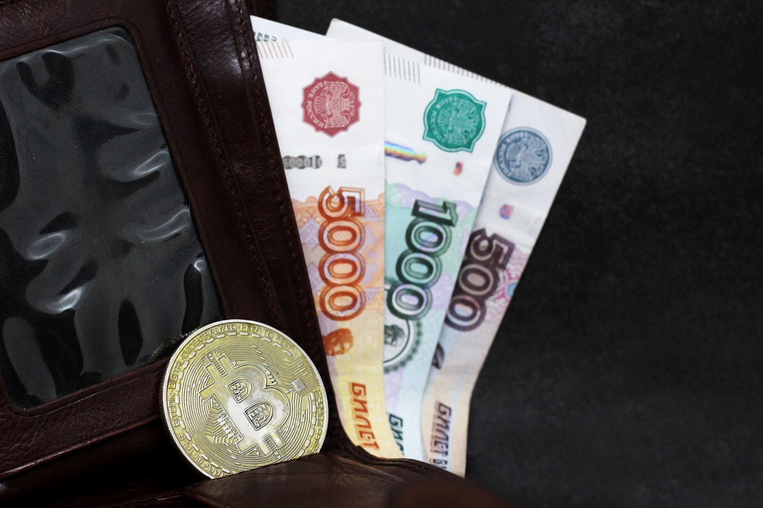 A wallet with protruding Russian ruble banknotes, as well as a metal token intended to represent Bitcoin