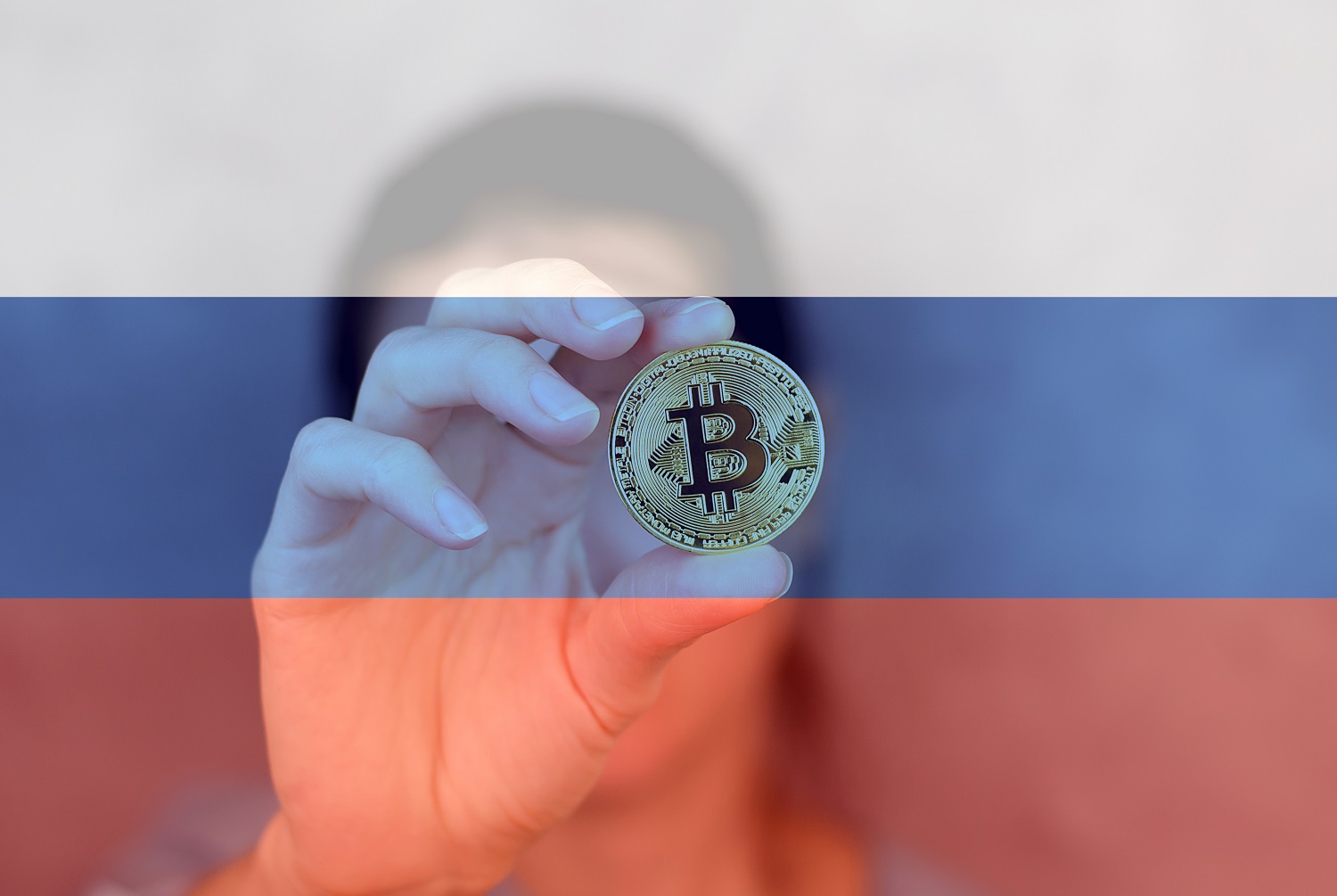 A person holds a metal token intended to represent Bitcoin against the backdrop of the Russian flag.