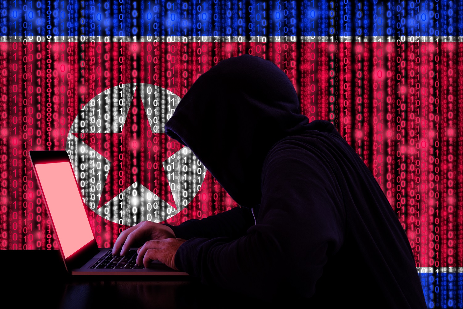 A hooded person works on a laptop against the backdrop of a North Korea flag composed of binary code.