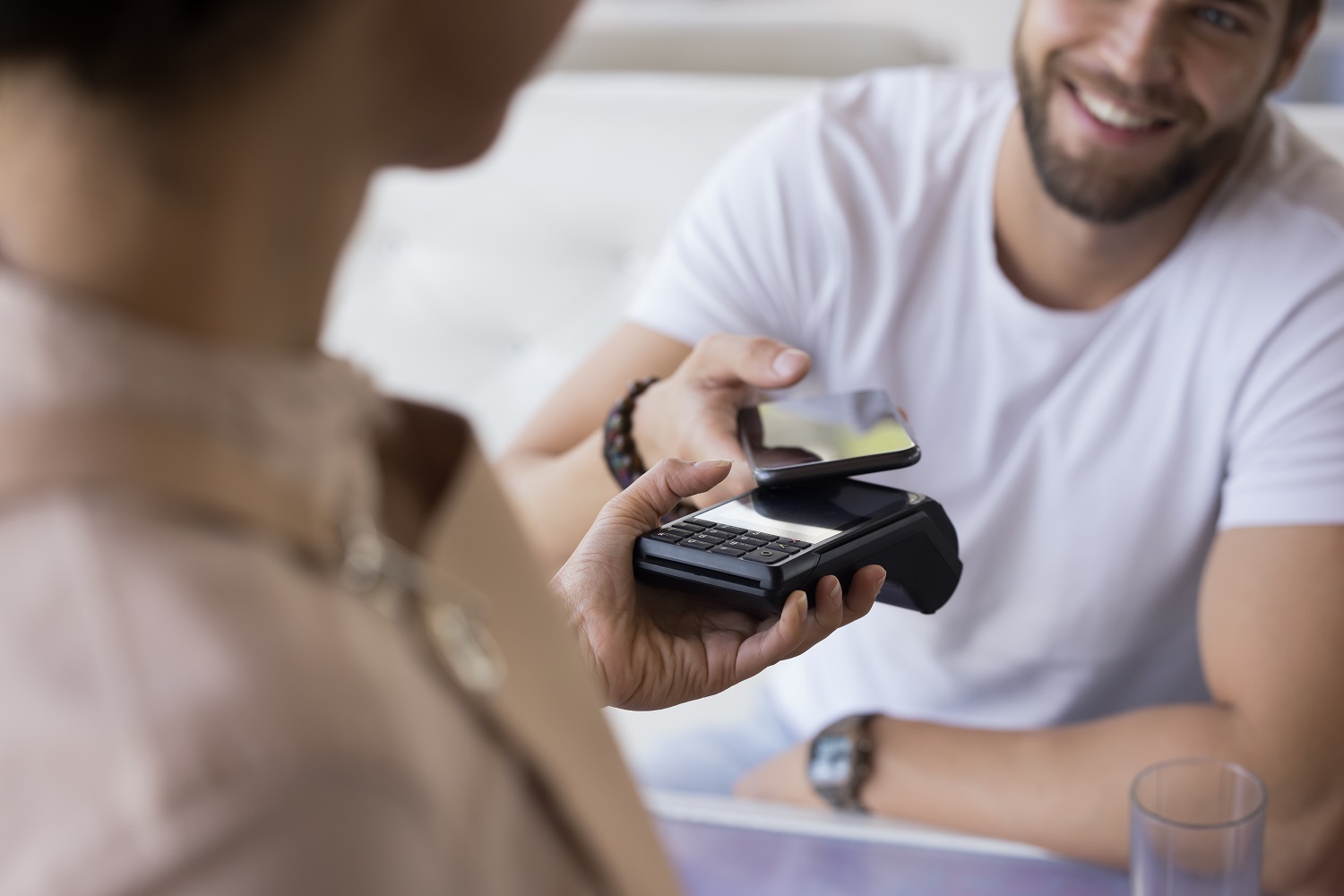 A male customer pays using a smartphone at a store as a clerk holds out a POS device.