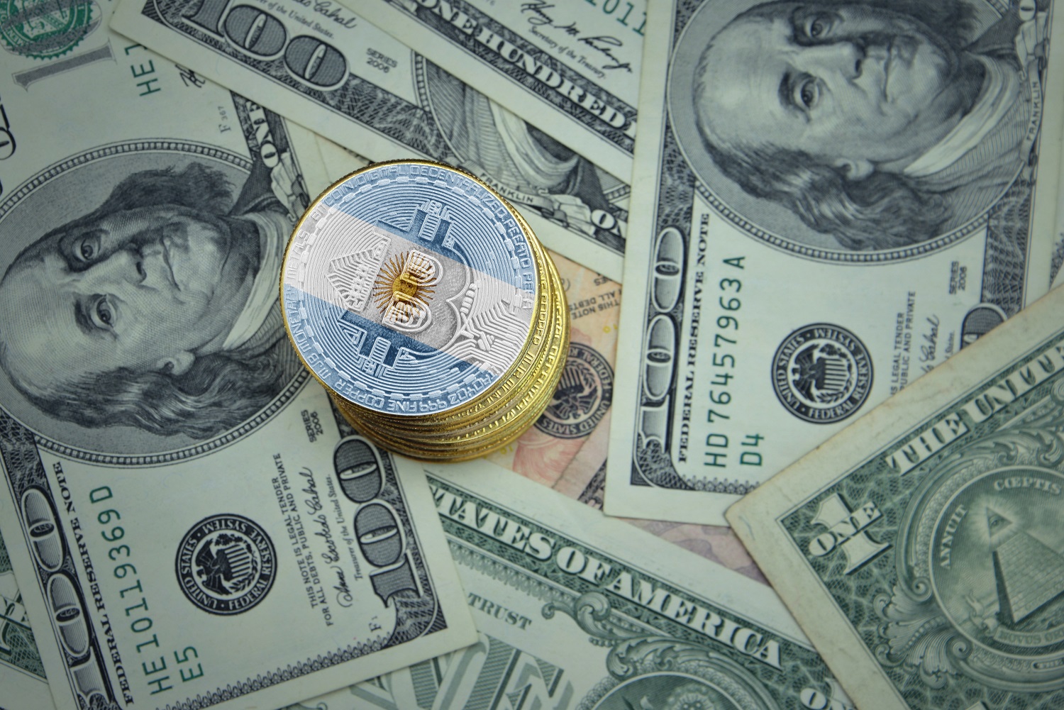 Một chồng thẻ kim loại nhằm đại diện cho Bitcoin được trang trí bằng màu cờ của Argentina nằm rải rác trên các tờ đô la.