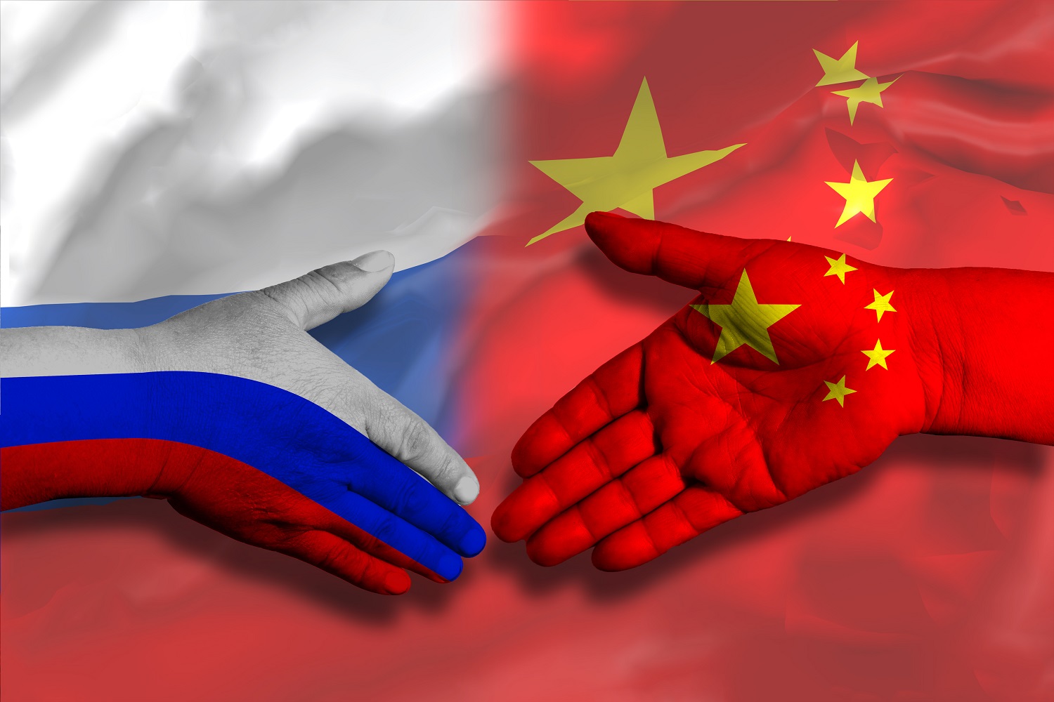 Two hands, one decorated in the colors of the Chinese flag and the other in the colors of the Russian flag, move together as if to shake hands against the backdrop of the flags of both countries.