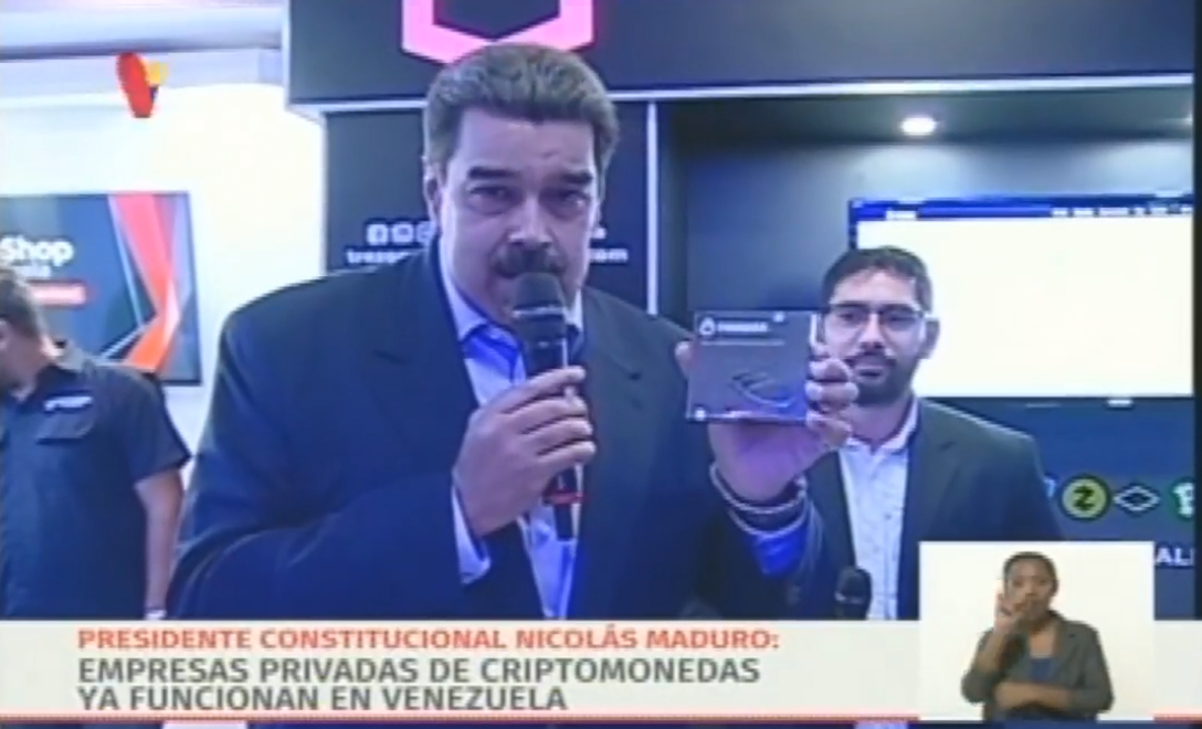 Venezuela's President Nicolás Maduro holds a crypto hardware wallet and speaks into a microphone.