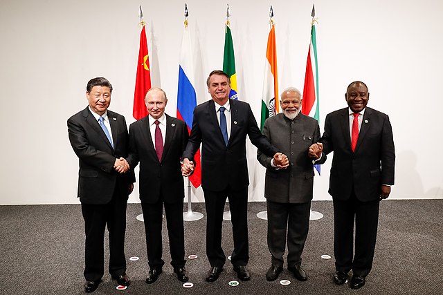 Năm nhà lãnh đạo của các quốc gia BRICS nắm tay nhau trước lá cờ của quốc gia họ tại một cuộc họp vào năm 2019.