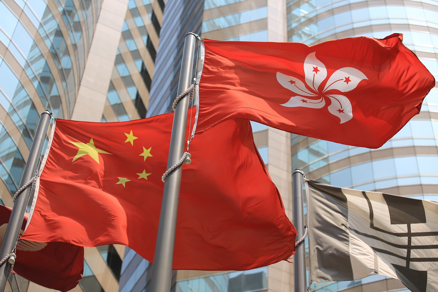The flags of China and Hong Kong, hoisted on flagpoles and blowing in the wind.