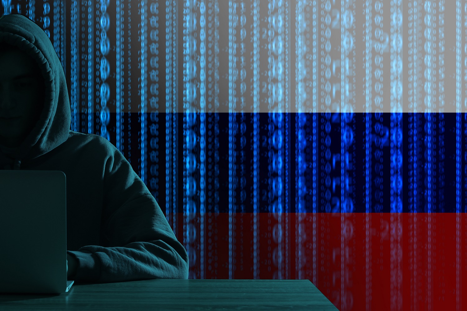 A silhouette of a hooded hacker with a laptop on a background decorated in the colors of the Russian flag.