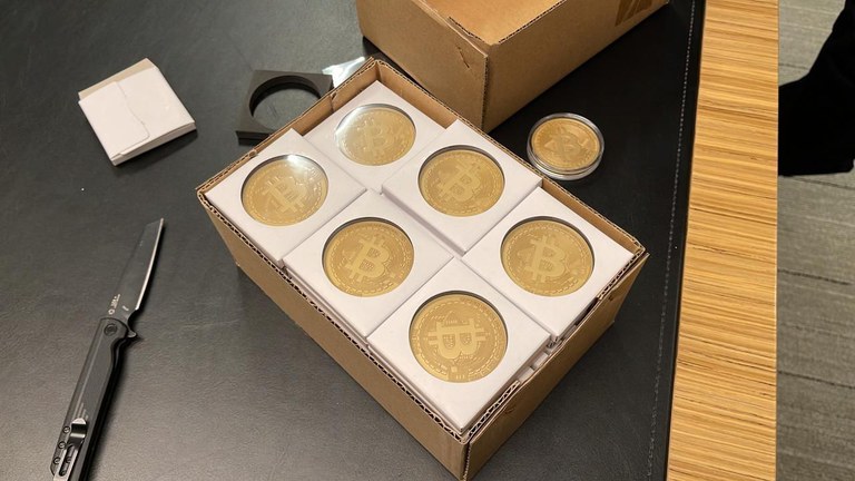 A box of what appears to be stickers featuring Bitcoin logos seized by Brazilian police, next to a box cutter.