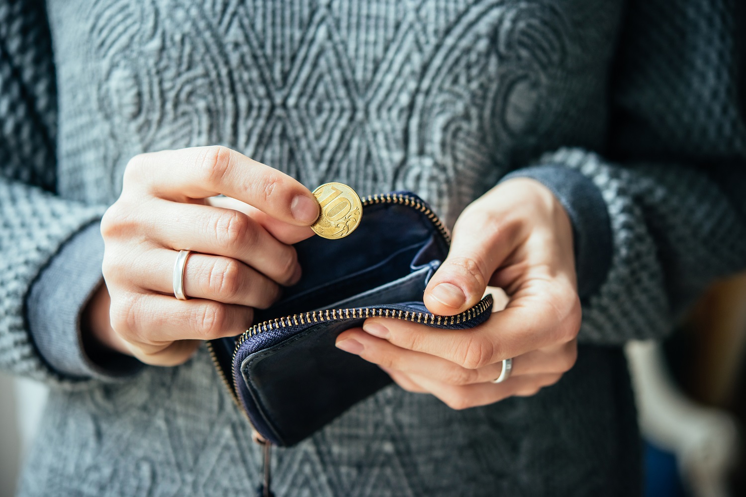 A person wearing a grey sweater removes a Russian coin from a black leather wallet.