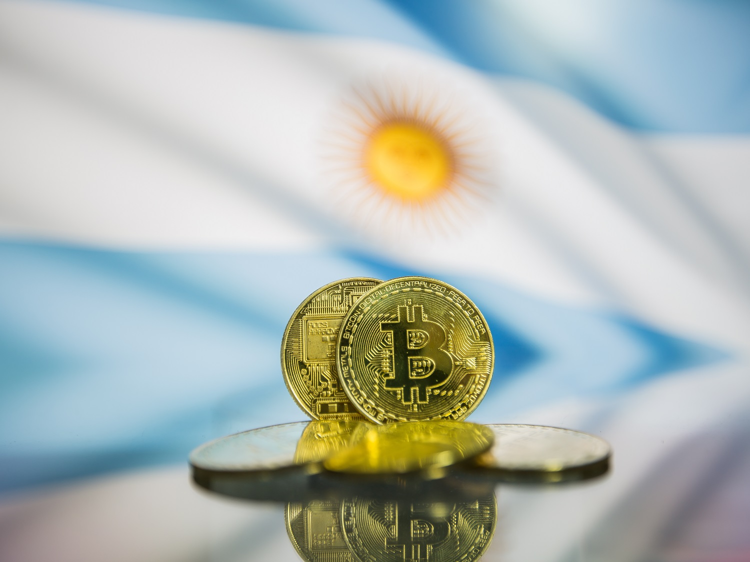 Five metal tokens intended to represent Bitcoin, against the backdrop of the Argentinian Flag.