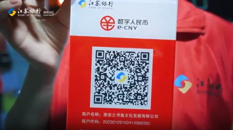 A bank employee holds a card embossed with a QR code and the e-CNY logo.