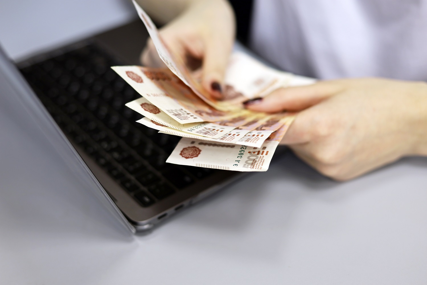 A close-up of a woman’s hands as she counts Russian ruble banknotes next to a laptop.