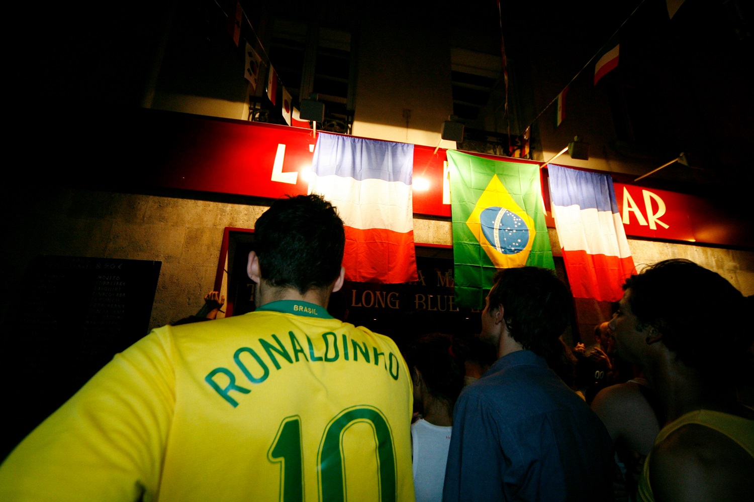Football (soccer fans) gather to watch a match between Brazil and France. One wears a Brazil national team uniform with the name Ronaldinho and the number 10 on the back.