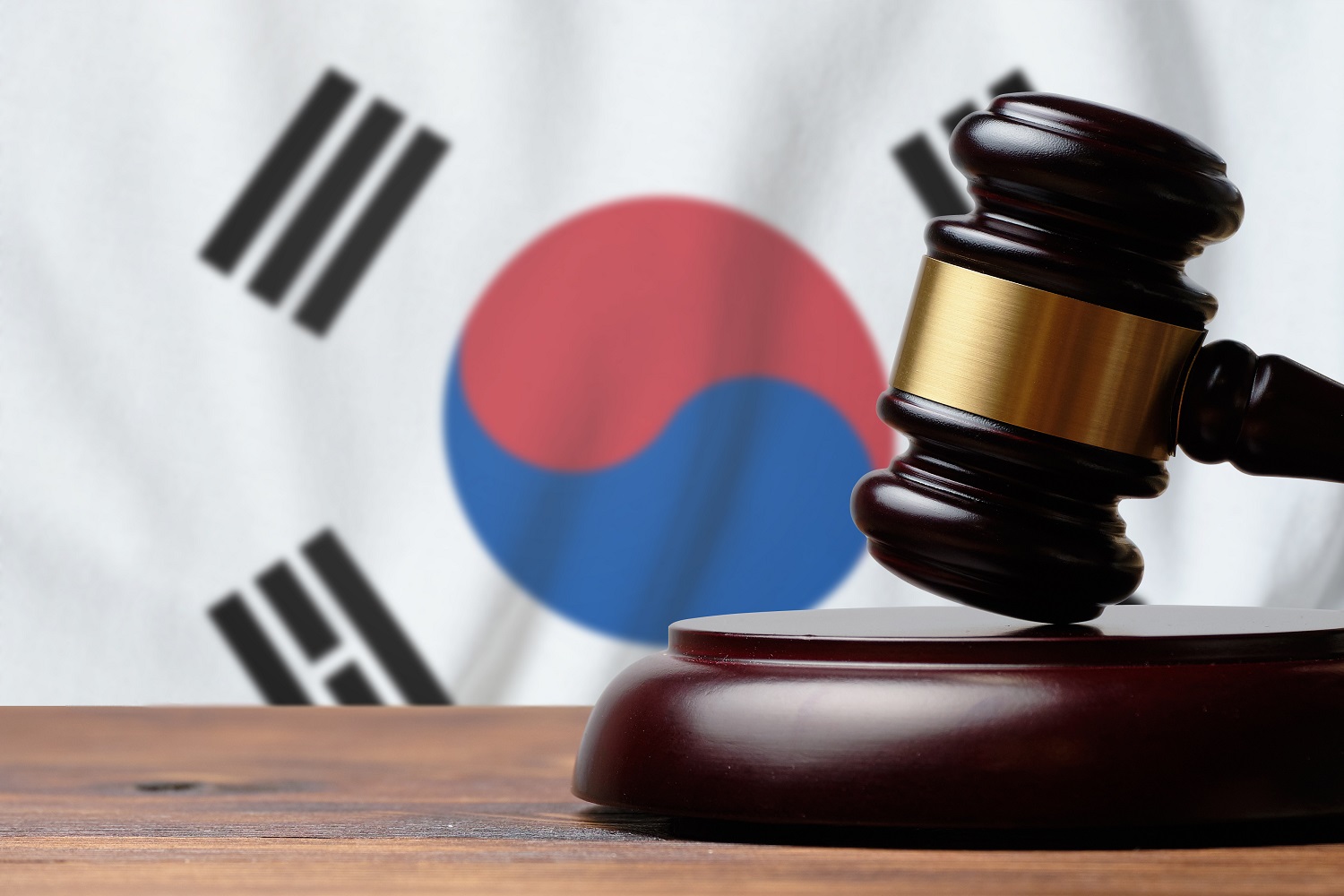 A gavel and block on a wooden desk against the background of a South Korean flag.