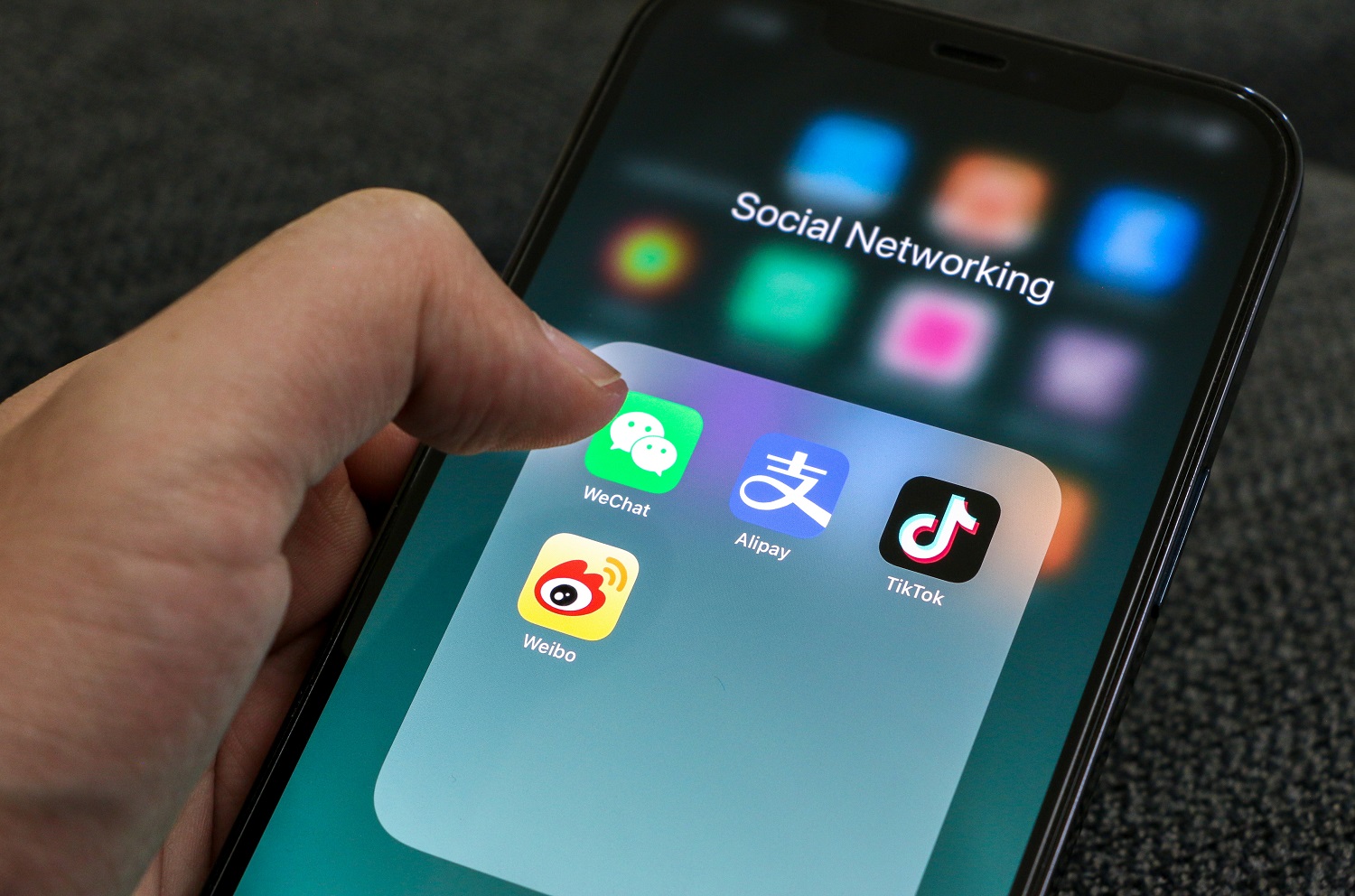 A person’s hand holds a mobile phone and is about to launch a Chinese social media app, with WeChat, Alipay, TikTok, and Weibo icons displayed.