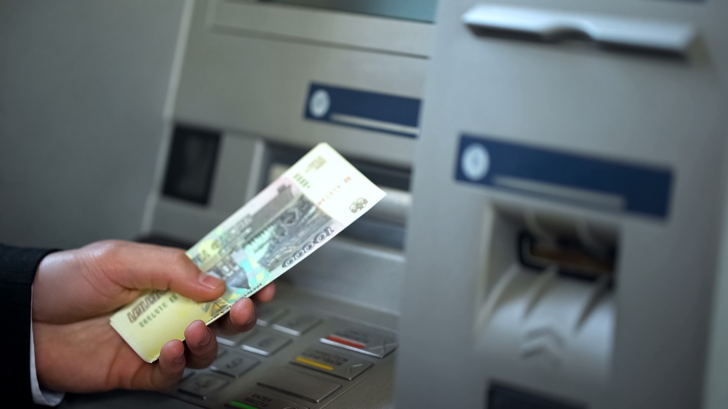 A man withdraws Russian ruble banknotes from an automatic teller machine.