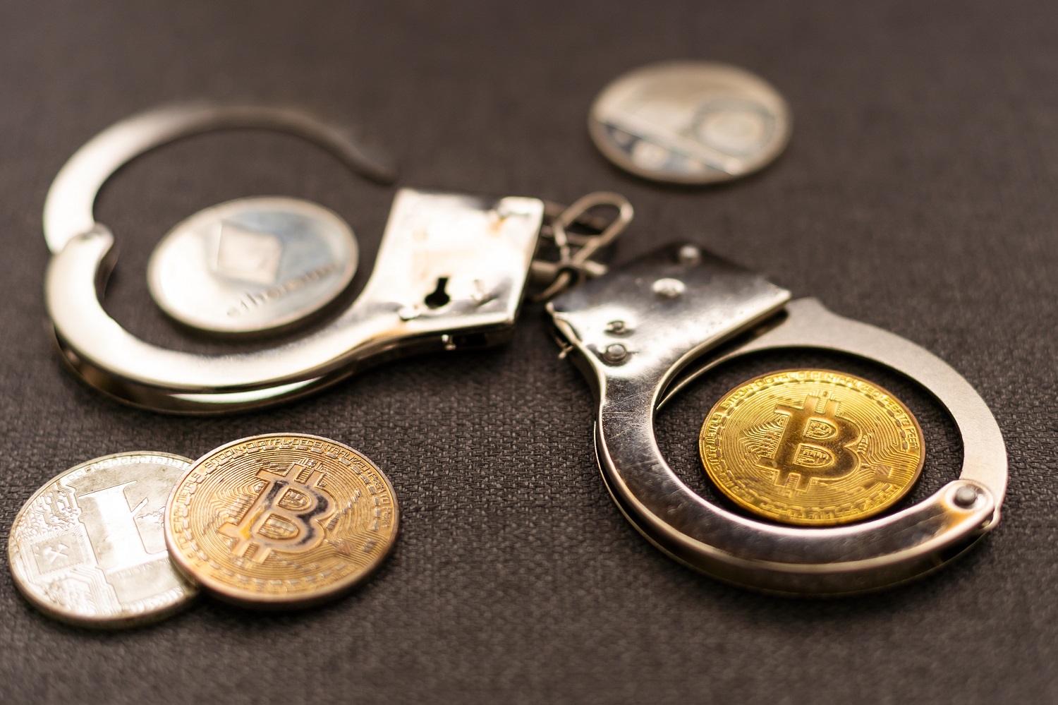 Tokens intended to represent cryptoassets such as Bitcoin, Ethereum, and Litecoin on a surface along with a pair of police handcuffs.