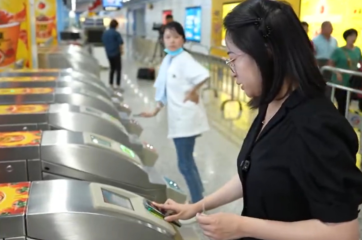 A Chinese TV news reporter uses the SIM card-based “hard wallet” on a powered-down smartphone to pay at a subway ticket barrier.