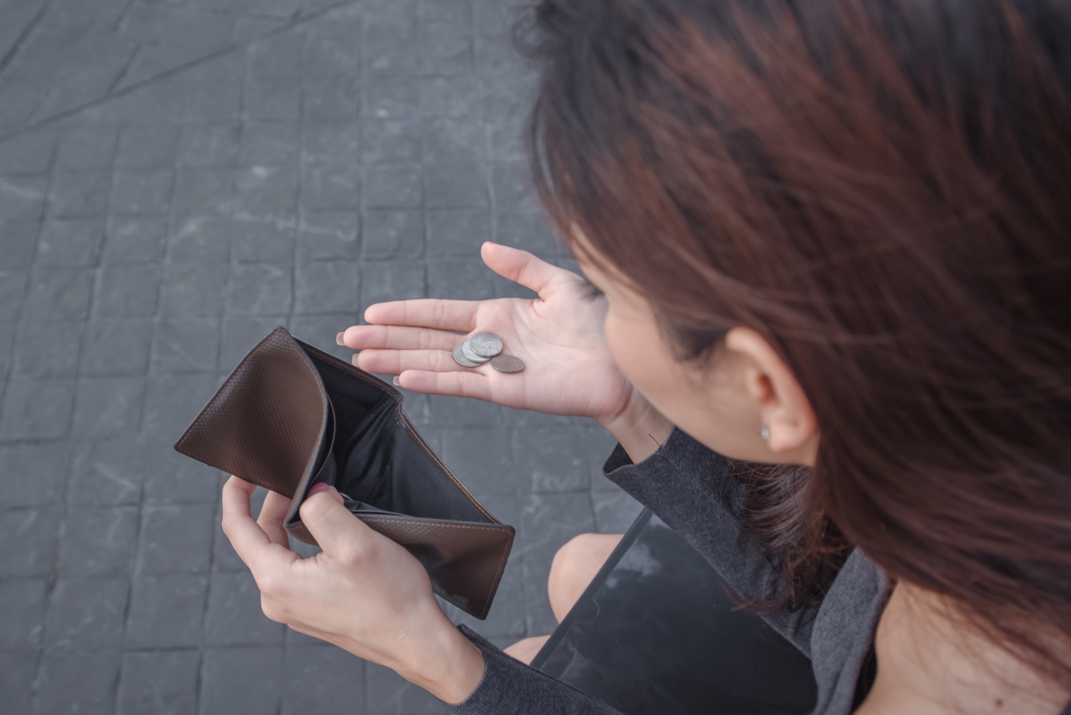 A woman holds a few coins in one hand and an empty wallet in the other.