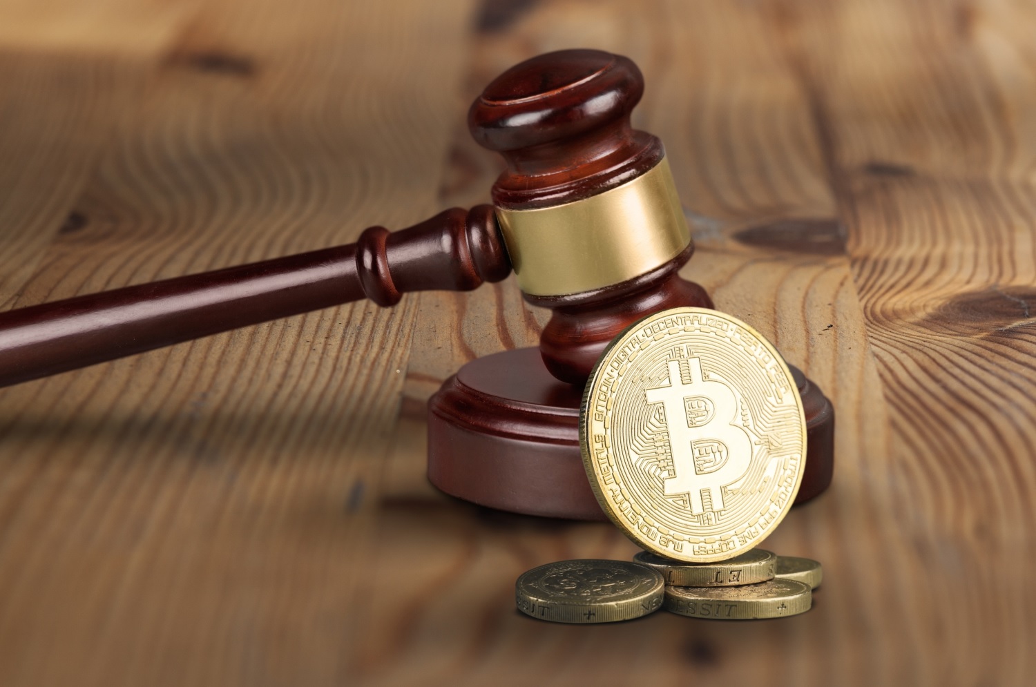 A judge’s gavel and block next to a small pile of metal coins, the largest of which is a token intended to represent Bitcoin.