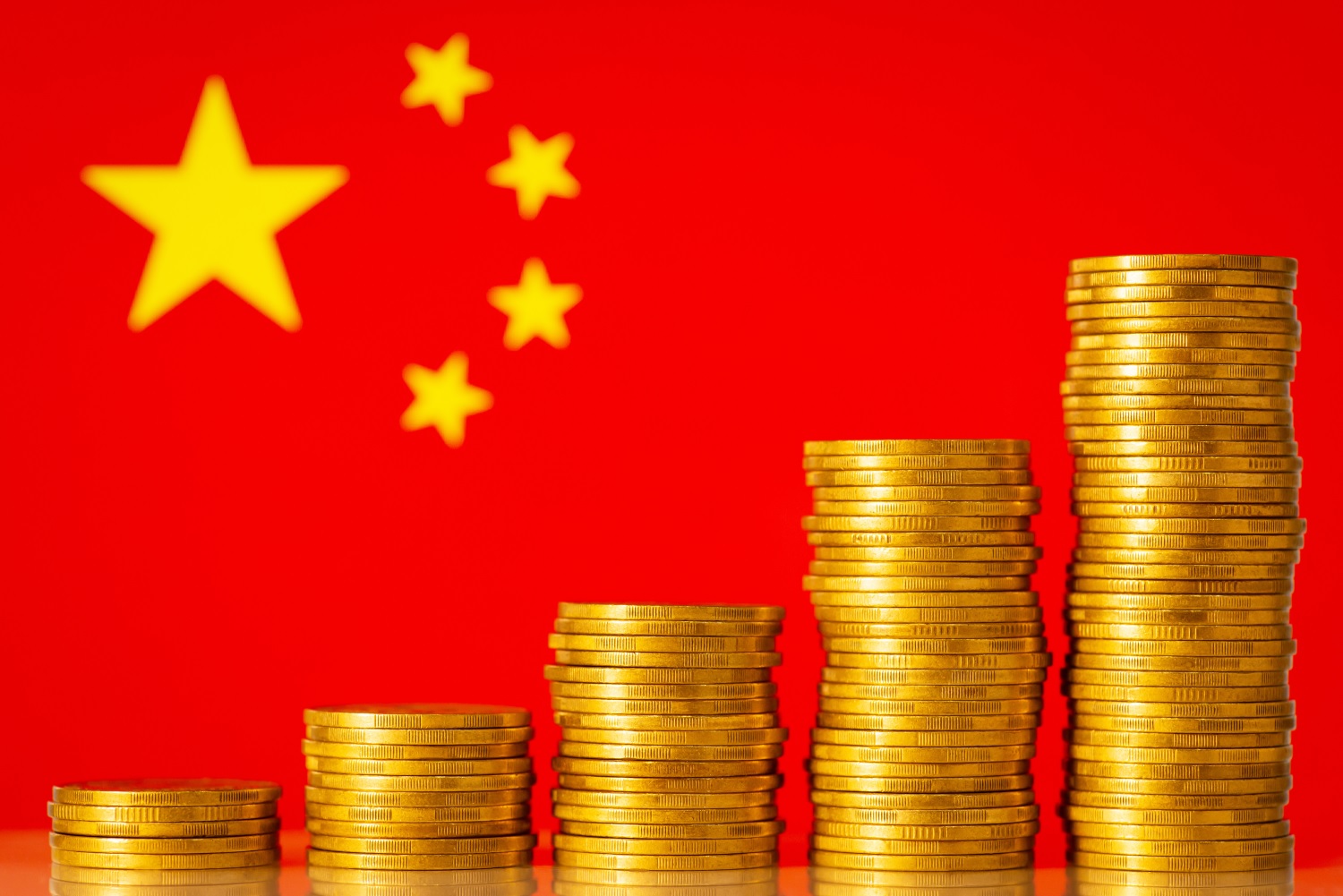 Five stacks of gold-colored coins against the backdrop of the flag of China.