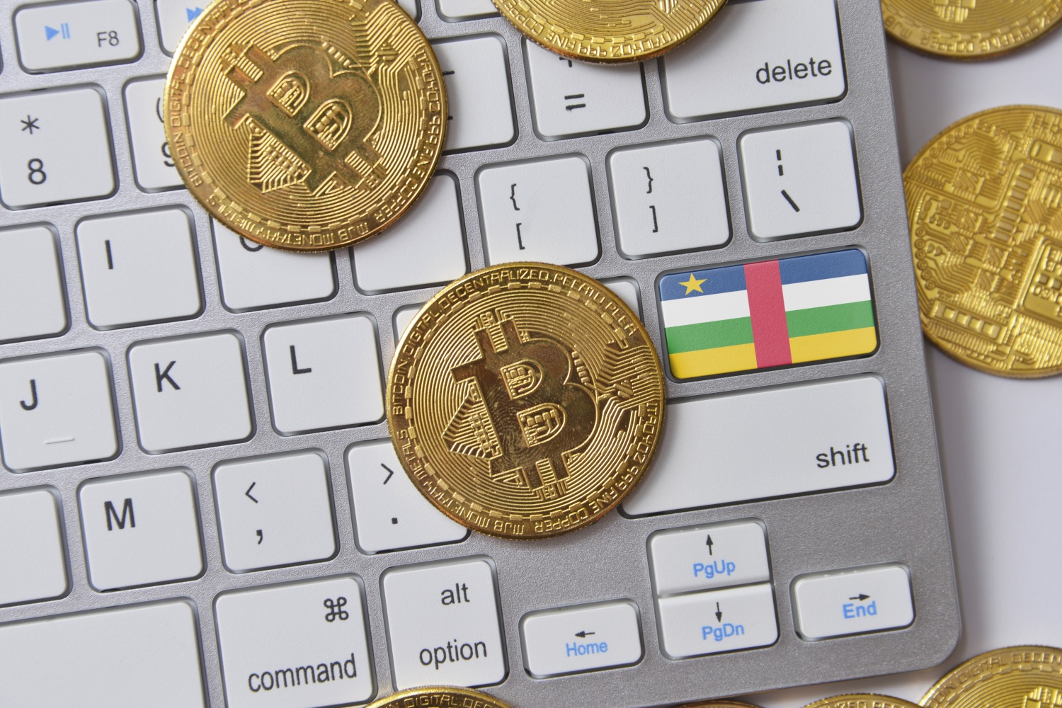 A keyboard whose Enter key is decorated in the colors of the flag of the Central African Republic. Several metal tokens, some of which are decorated with the Bitcoin logo, rest on and next to the keyboard.