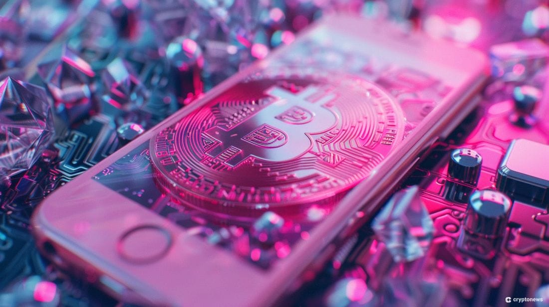 This image depicts a gold Bitcoin coin resting on a smartphone, against a vibrant pink and blue background with scattered crystals. The image alludes to the integration of cryptocurrency into everyday life, a concept explored by artists like Iggy Azalea, who has recently launched her own crypto token.