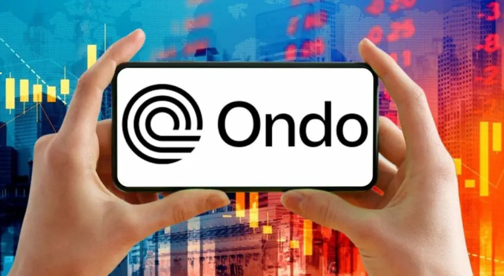 A person holding a phone displaying the Ondo Finance logo against a financial background.