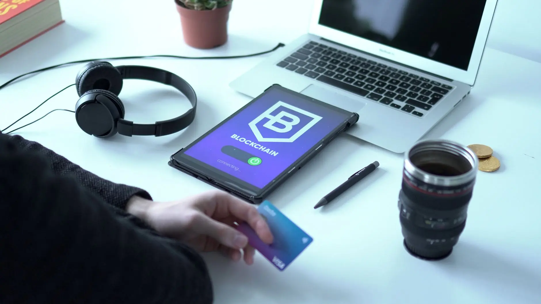 A person holding a credit card next to a tablet displaying a blockchain interface.