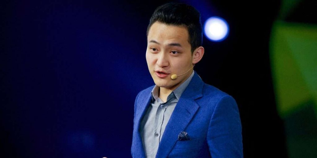 Man in blue suit speaking on stage with a headset microphone.