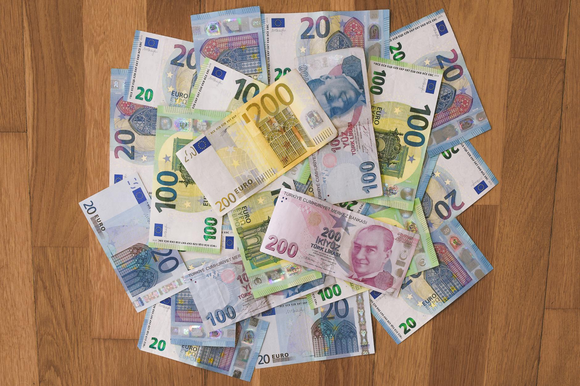 Pile of various Euro and Turkish Lira banknotes on a wooden surface.