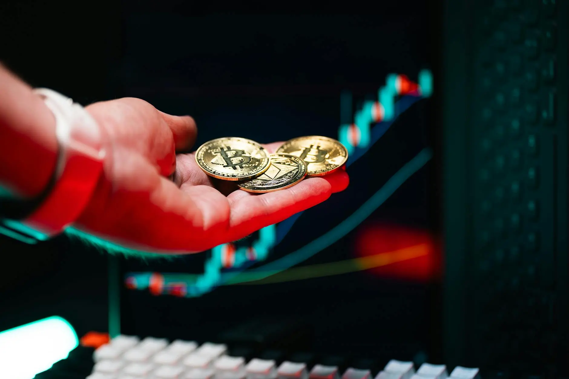 Hand holding three Bitcoin and Ethereum coins with a colorful chart in the background.