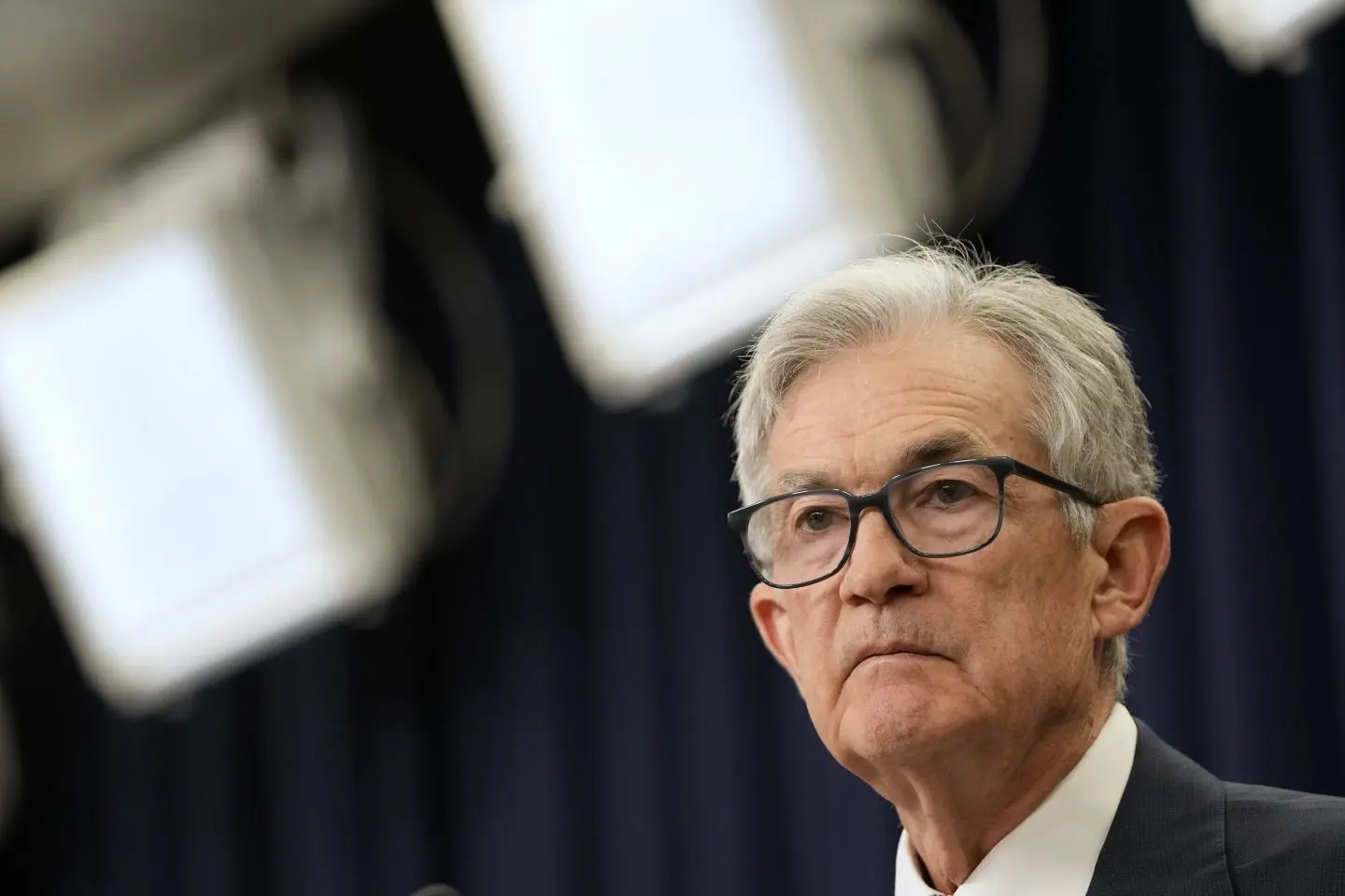 Jerome Powell speaks at a press conference with lights in the background.