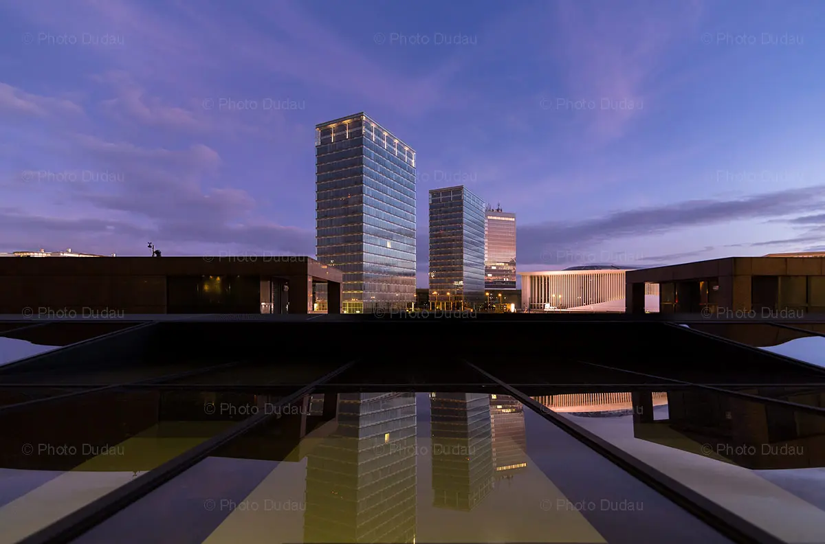 Modern glass skyscrapers and a reflective surface in Kirchberg, Luxembourg at dusk.
