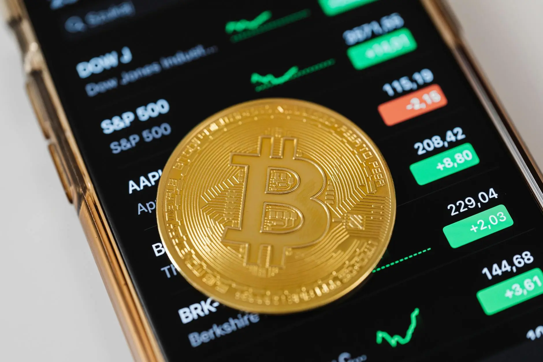 A smartphone displaying stock market data with a Bitcoin coin on top.