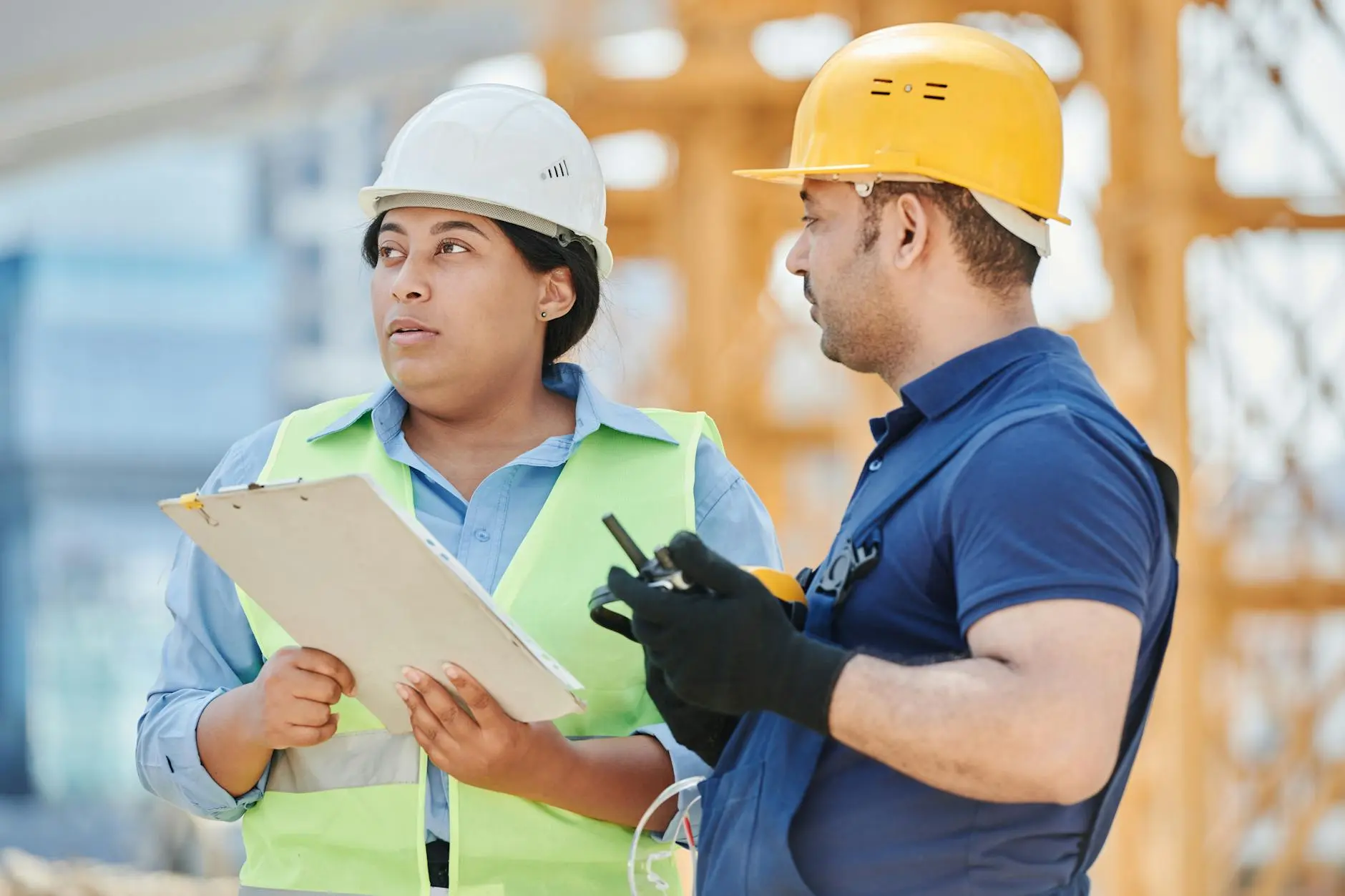 Two construction workers discussing with a clipboard and radio at a site.