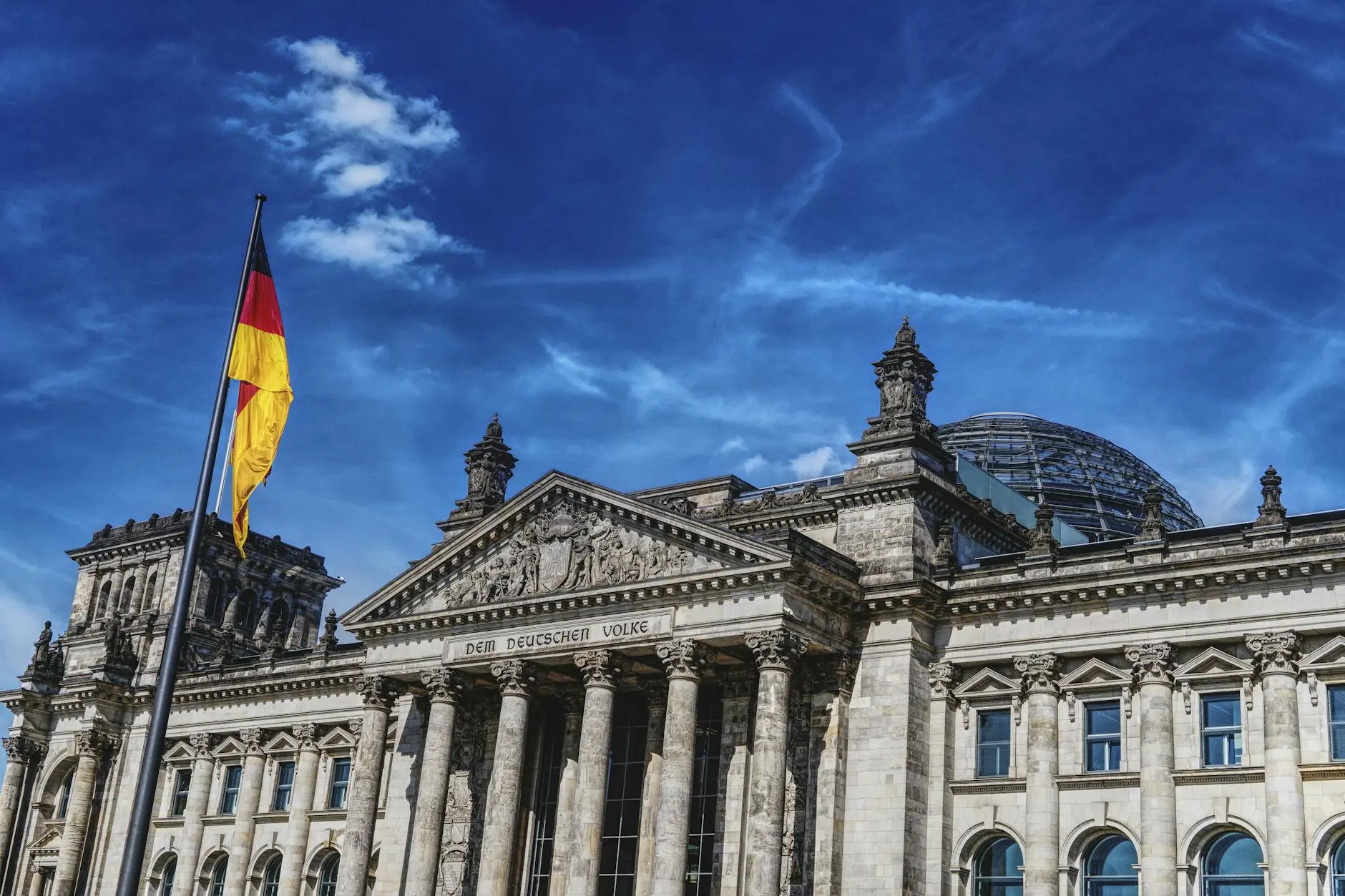 The Reichstag building in Berlin, Germany, with a German flag and blue sky.
