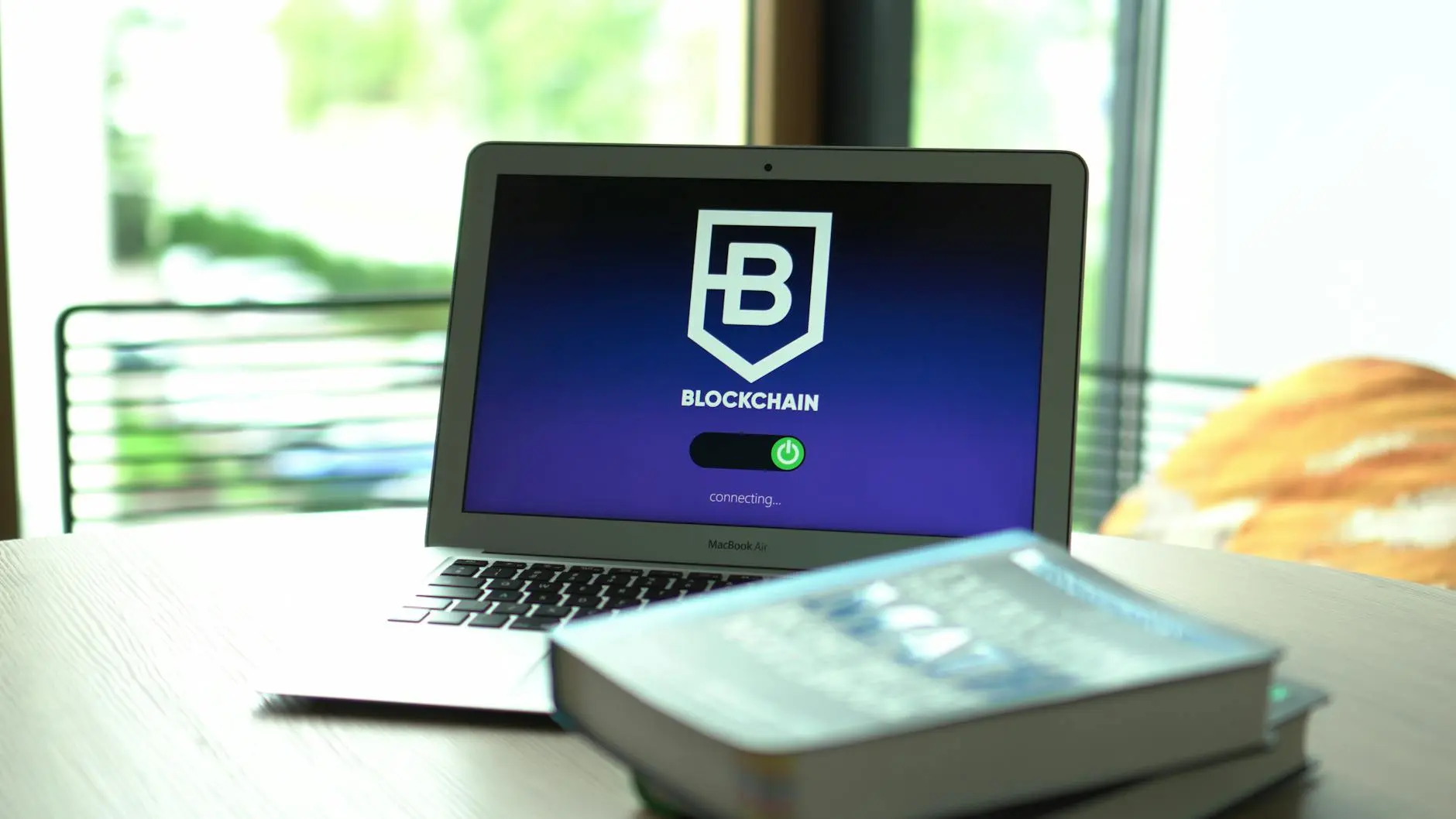 A laptop displaying a blockchain interface, with books on a wooden table.