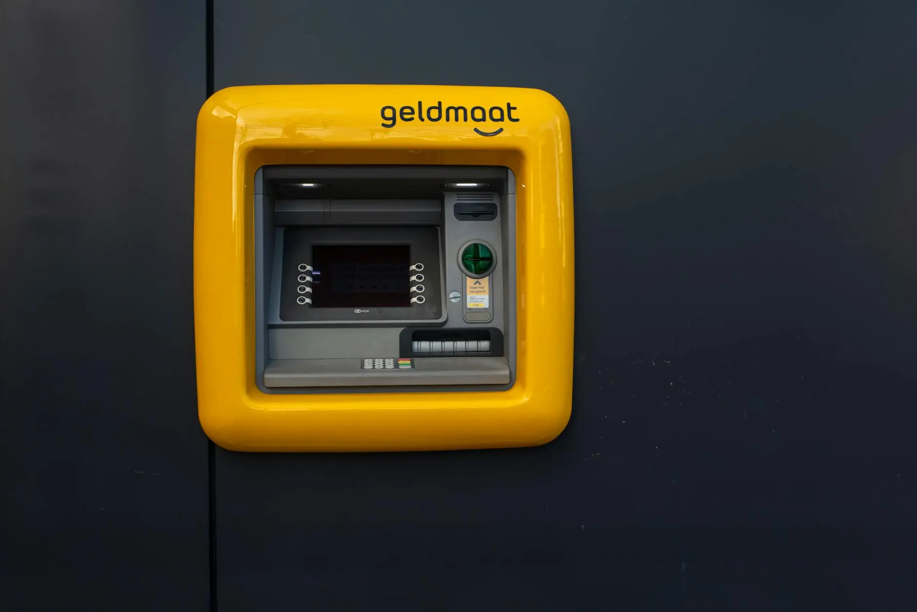 A bright yellow ATM machine labeled 'geldmaat' on a dark background.