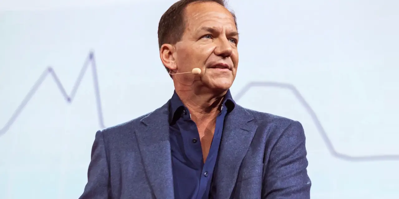 Paul Tudor Jones speaking at an event, wearing a blue suit and microphone.