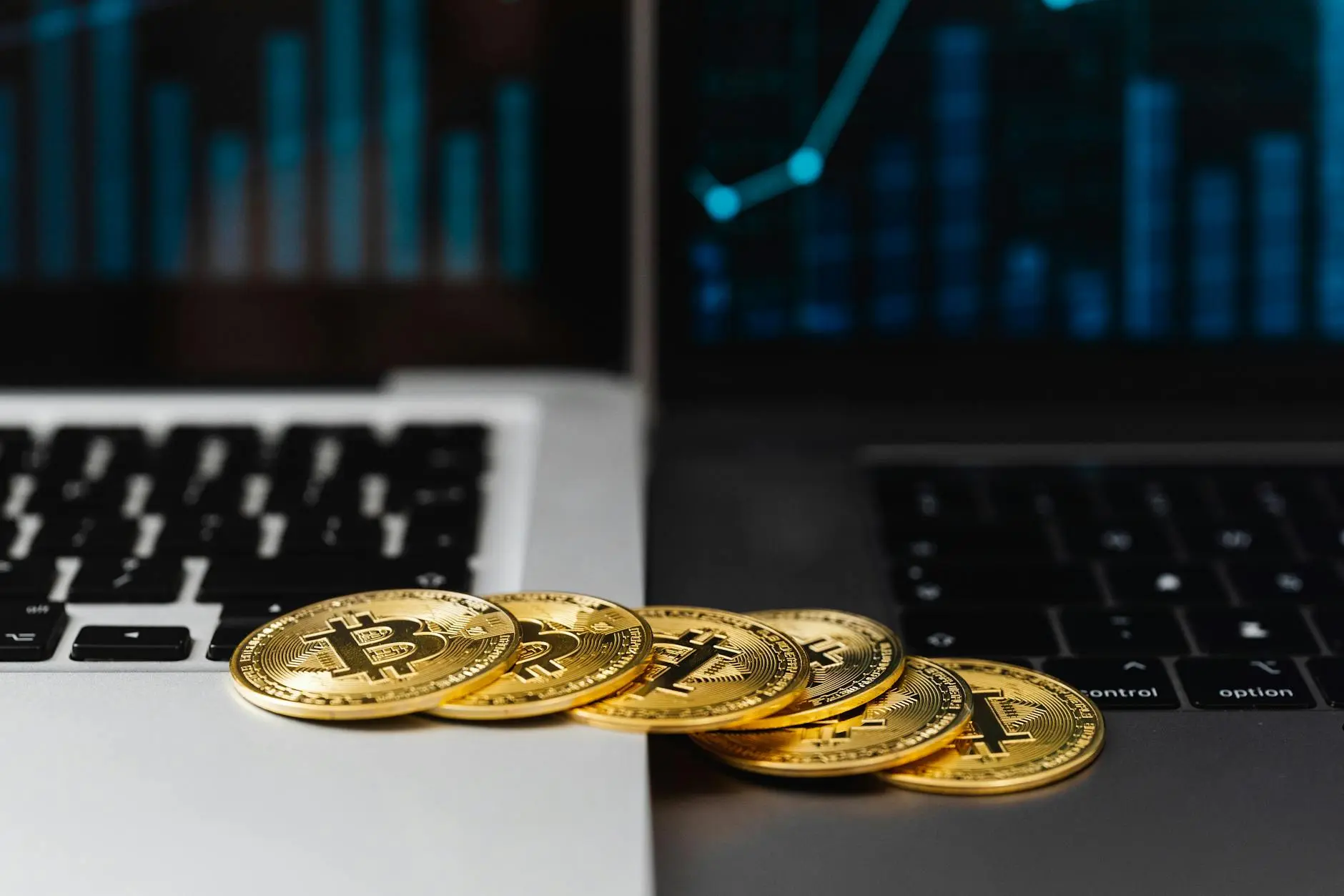Gold Bitcoin coins on a laptop keyboard with financial graphs on the screen.