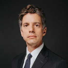 Professional headshot of a man in a suit against a dark background.