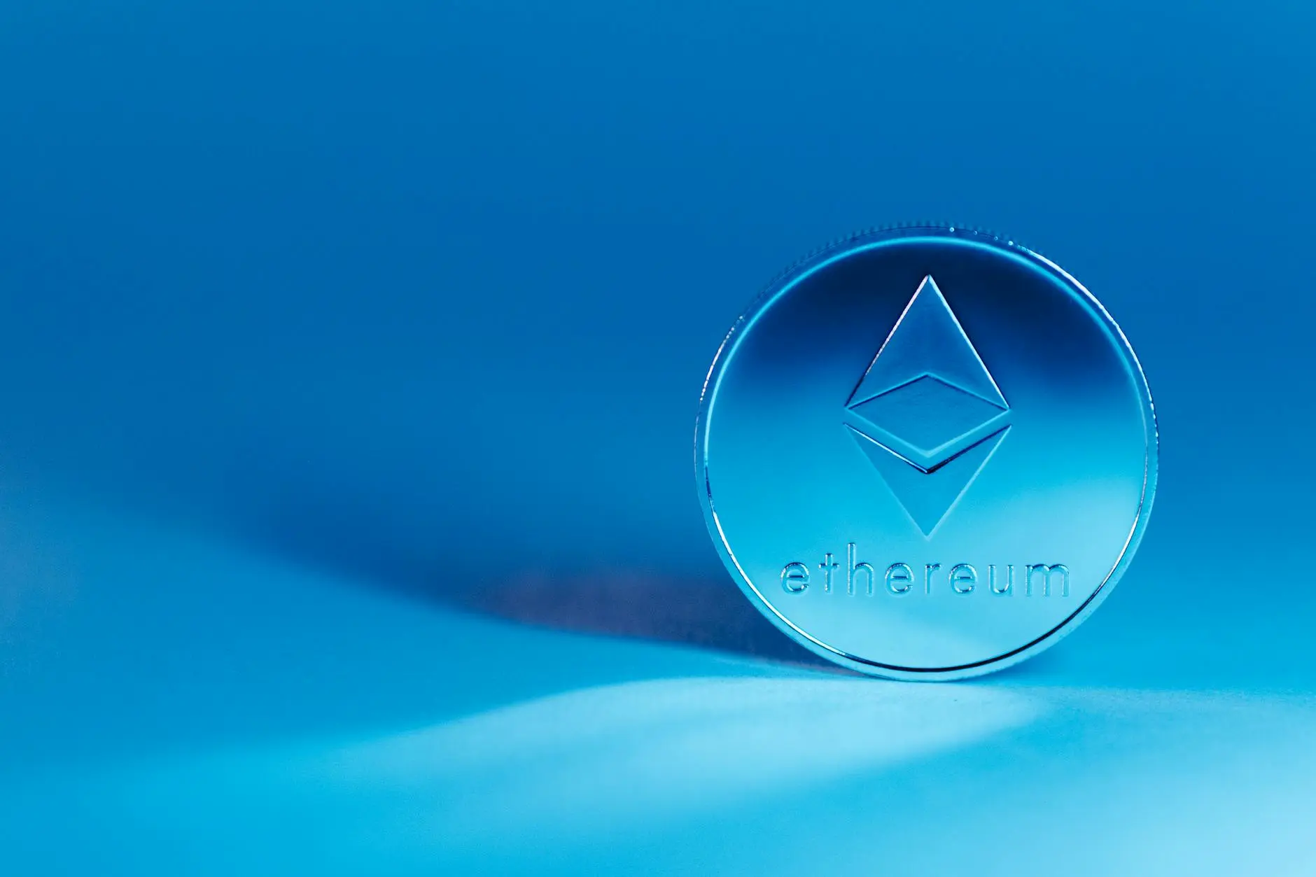 A silver Ethereum coin displayed on a soft blue background.