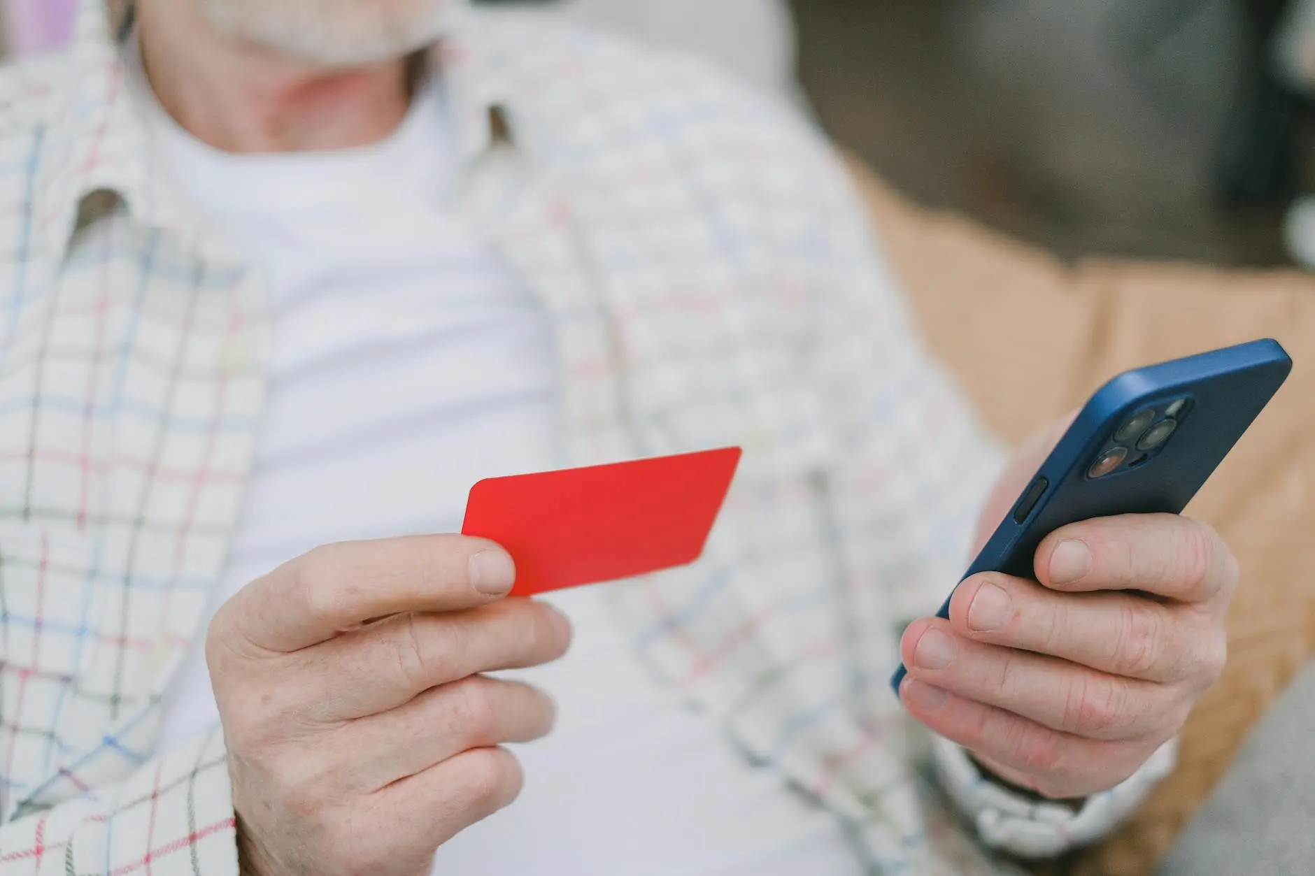 An older man holds a red card in one hand and a smartphone in the other, seated indoors.