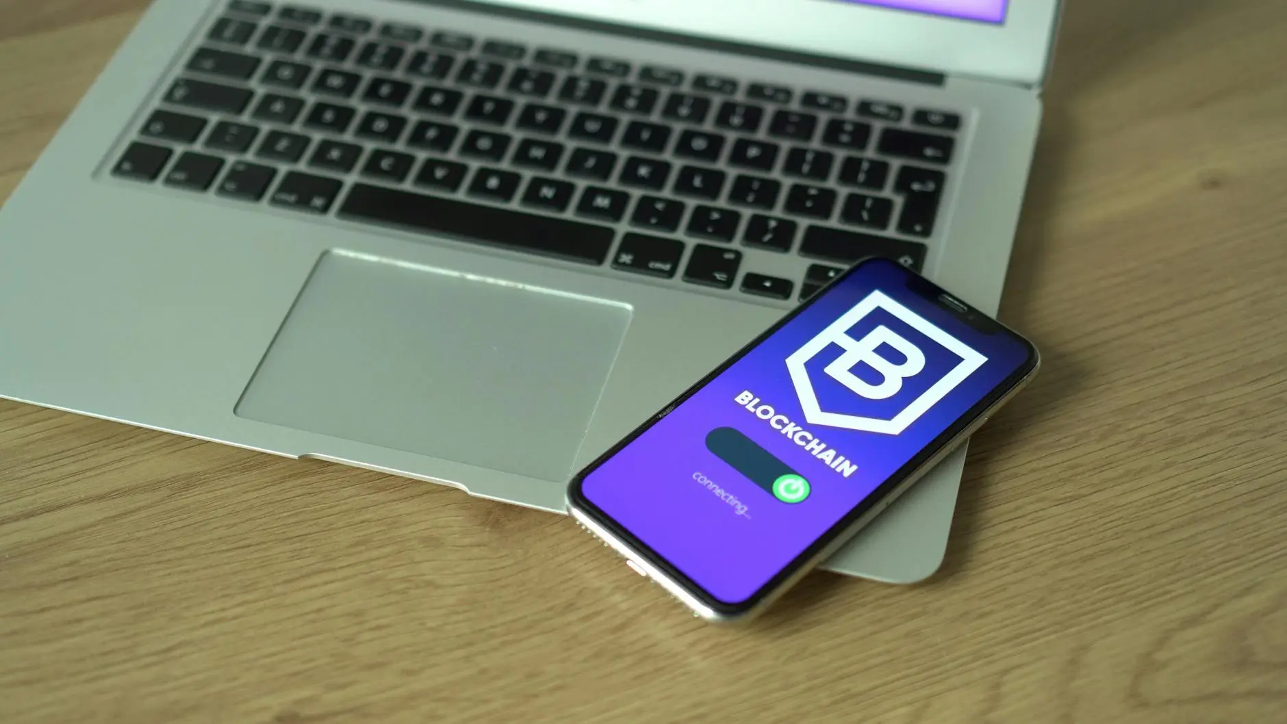Smartphone displaying a blockchain app on a wooden table next to a laptop.